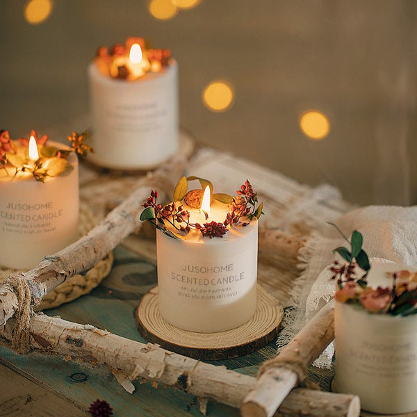 Four lit Luxury Scented Candles—Dry Flower Pure Soy Wax with Natural Cotton Wicks—sit in white jars on a rustic wooden tray, dried flowers atop each, as warm fairy lights softly glow in the background, creating a cozy aromatherapy ambiance.