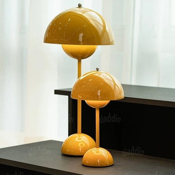 Two yellow Large Bud Table Lamps | Plug-In Edition with Cast Iron Base, each at a different height, are placed on a black surface in front of a white curtain.