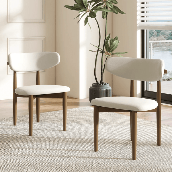 A set of two Mid-Century Modern Dining Chairs, featuring solid wood frames and custom upholstery options, are arranged on a light rug by a potted plant and window in a bright, minimalist room.