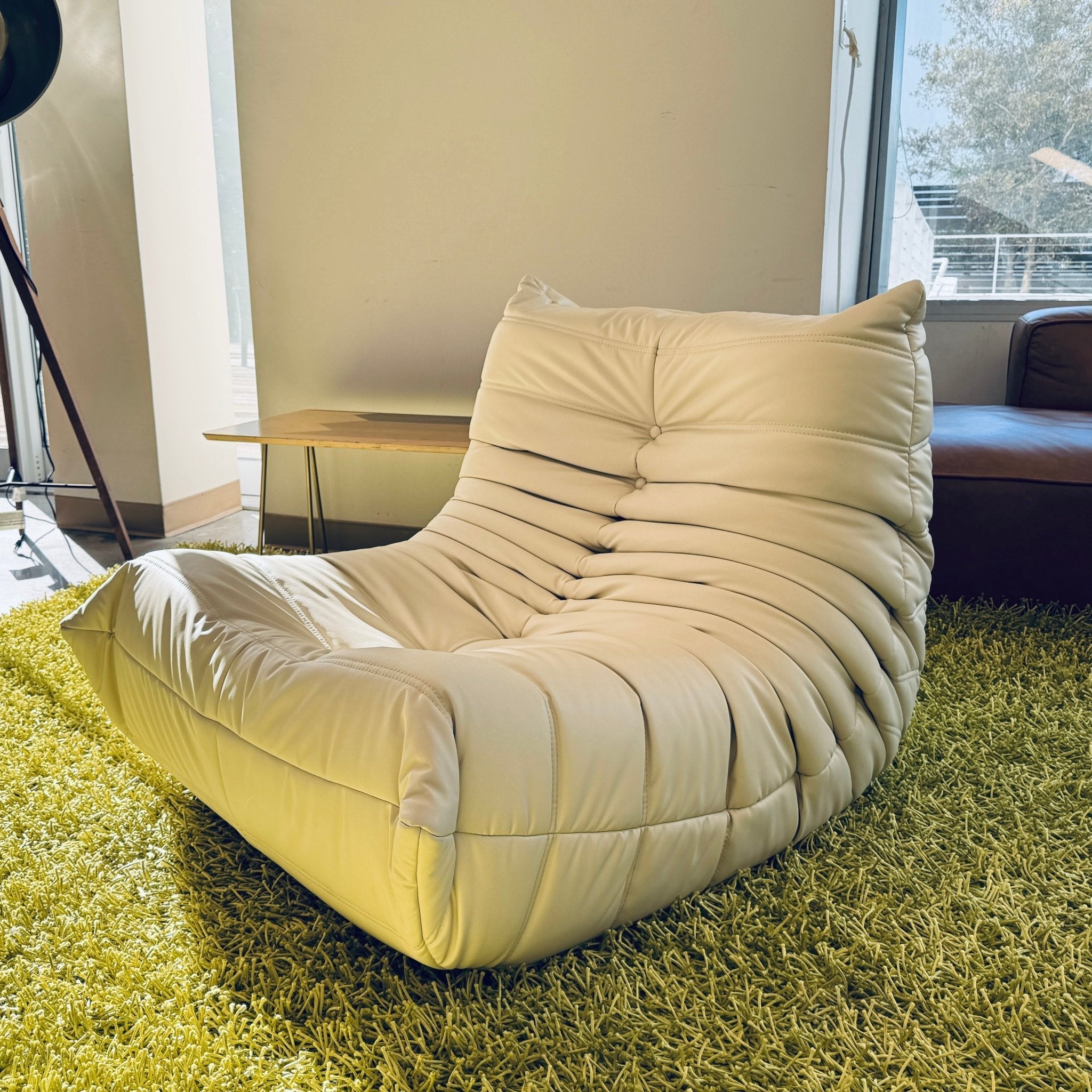The Chillax Lounger Sofa Chair, with its modern tufted design, offers a luxurious lounging experience on a green shag carpet in a bright room near a window.